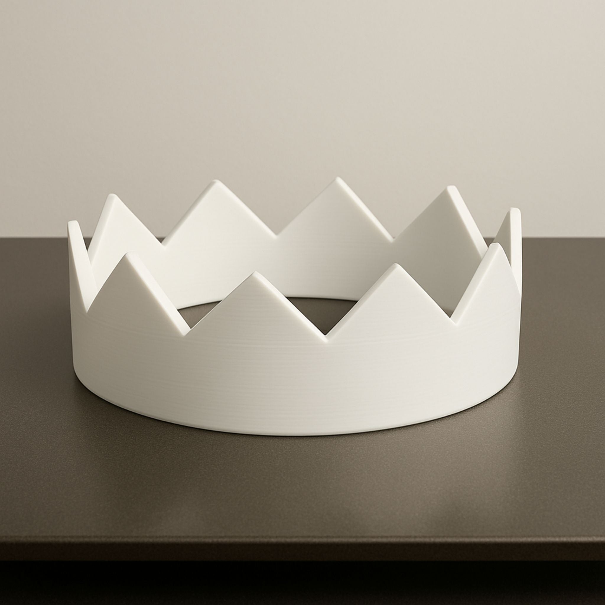 White crown-shaped object on a dark surface with a neutral background