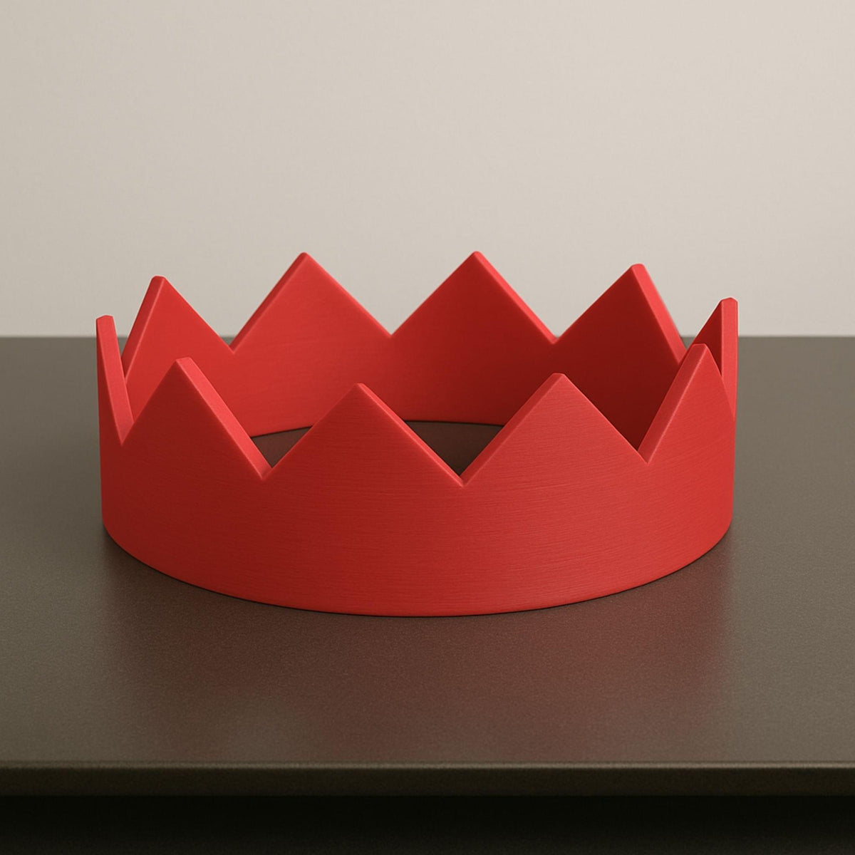 Red crown-shaped object on a dark surface with a neutral background